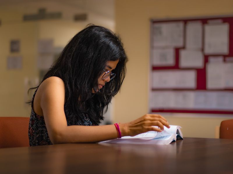 An Indian student studying a textbook in a library